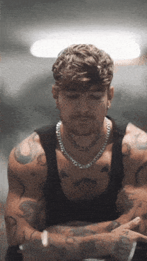 a man with a necklace around his neck has a tattoo of a laurel wreath on his chest