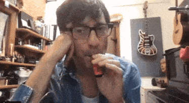 a man with glasses is drinking from a red bottle