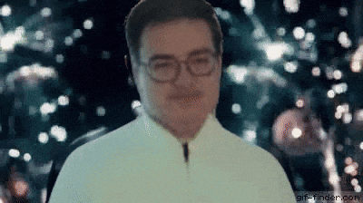 a man wearing glasses is standing in front of a christmas tree in the dark .