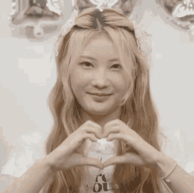 a girl with long blonde hair is making a heart shape with her hands .