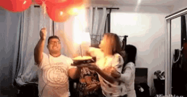 a man and woman are holding a cake and balloons in a room .