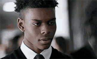 a young man in a black sweater and tie is looking at the camera .