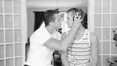 two men are kissing while wearing headphones in a black and white photo .