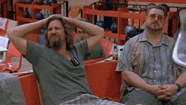 two men are sitting in a bowling alley with their hands on their head