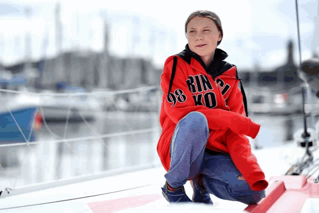 a woman wearing a red rin 98 ko sweatshirt is squatting on a boat