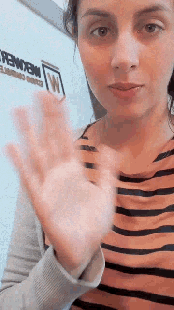 a woman in a striped shirt waves her hand in front of a wall that says " mekomer "