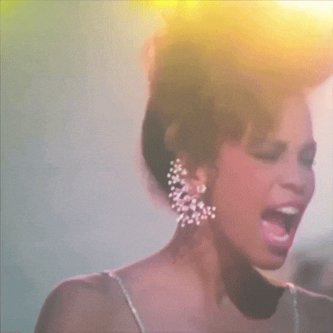 a woman wearing a white dress and earrings is singing into a microphone