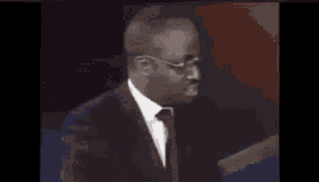 a man in a suit and tie is standing in front of a microphone in a dark room .