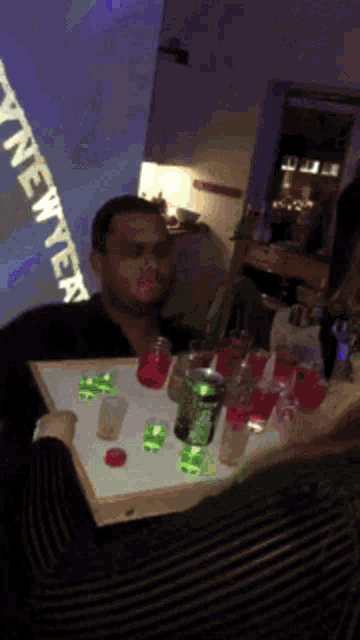 a man is sitting at a table with a tray of shot glasses and a sign that says wine week
