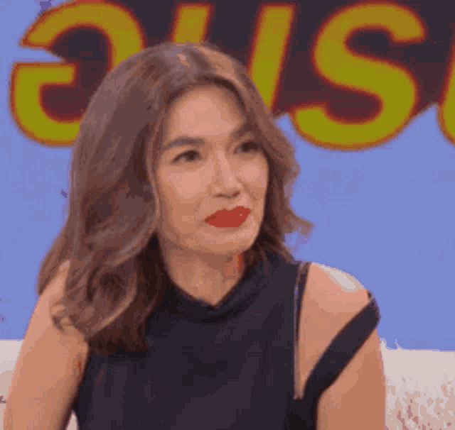 a woman wearing red lipstick is sitting on a couch in front of a sign that says ' s ' on it