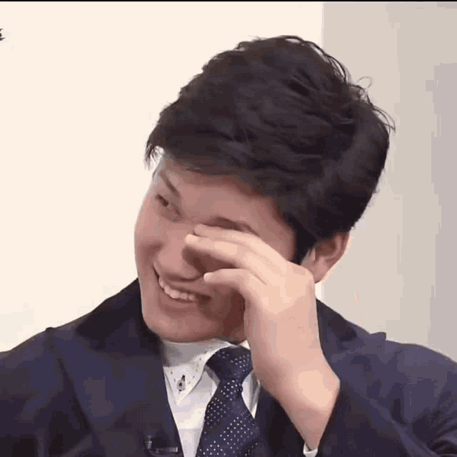 a man wearing a suit and tie is covering his face with his hand .
