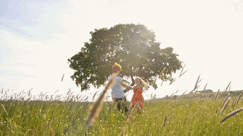 a boy and a girl are playing in a field with a tree in the background