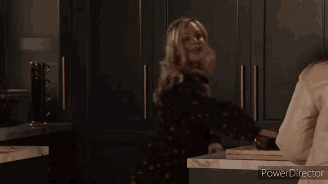 a woman is standing in a kitchen talking to another woman who is holding a knife .