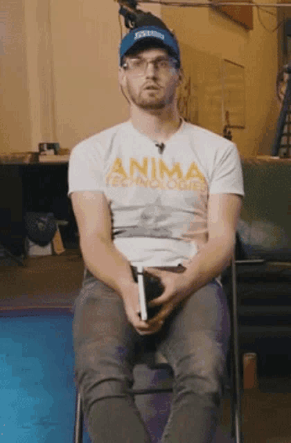 a man wearing a white shirt that says anima technologies sits in a chair