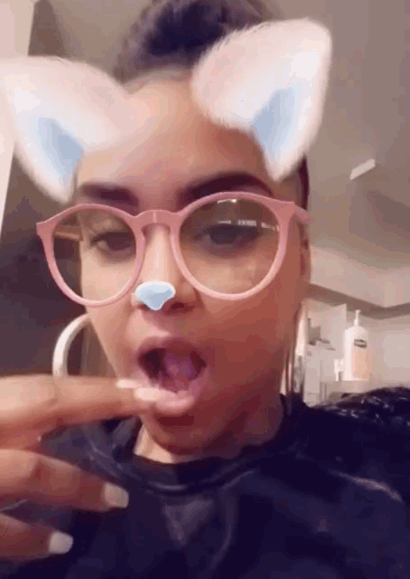 a woman wearing cat ears and glasses is licking her fingers