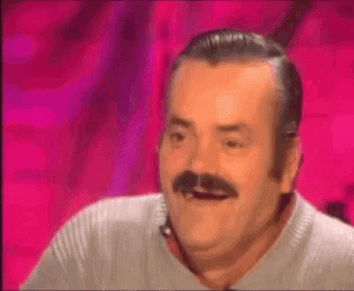 a man with a mustache is making a funny face while sitting in front of a pink background .