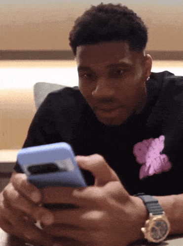a man wearing a black shirt with a pink teddy bear on it looks at his phone