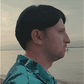 a man wearing a blue shirt with palm trees on it looks out over the water