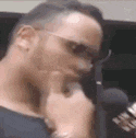 a man wearing sunglasses is talking into a microphone while holding his hand to his chin .