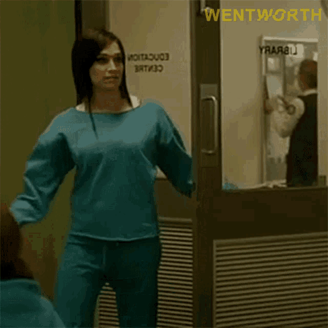 a woman in a blue sweater is standing in front of a door and says you 're here