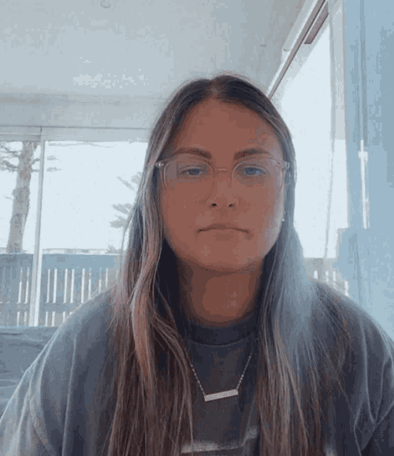 a woman wearing glasses and a necklace looks at the camera with a serious look on her face