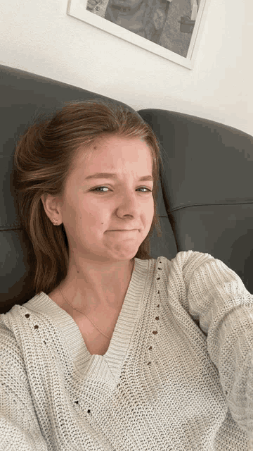 a woman in a white sweater is sitting on a couch and making a funny face