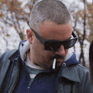 a man wearing sunglasses and a blue jacket is smoking a cigarette