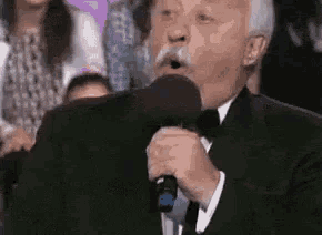 a man in a tuxedo is singing into a microphone in front of a crowd .