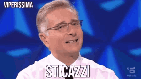a man wearing glasses and a white shirt is smiling and says sticazzi