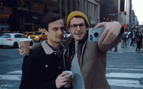 a man taking a selfie with another man holding a coffee cup