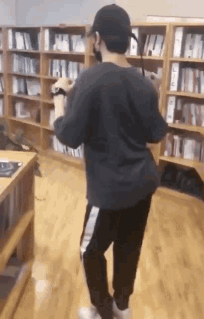a man is dancing in a library while wearing a hat and a mask .