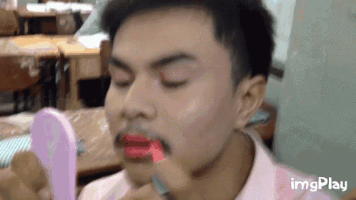 a man with a mustache is applying red lipstick to his lips while looking at himself in a mirror .