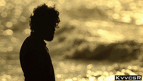 a silhouette of a man with a beard stands in front of a body of water
