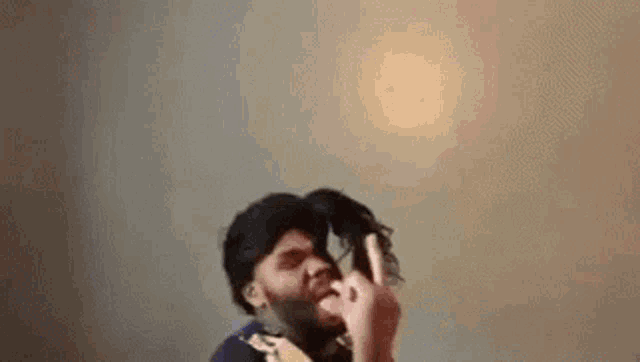 a man with a beard is holding a wig in front of his face and giving the middle finger .