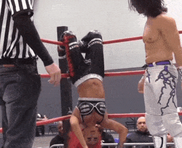 a wrestler is upside down in a ring with a referee watching