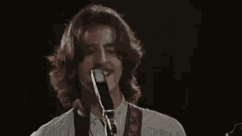 a man with long hair is singing into a microphone while holding a guitar .