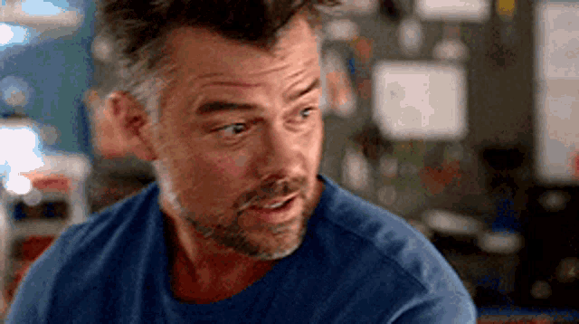a man with a beard and a mohawk is wearing a blue shirt and looking at the camera .