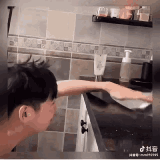 a man washing his face in a bathroom with a tube of lotion on the counter