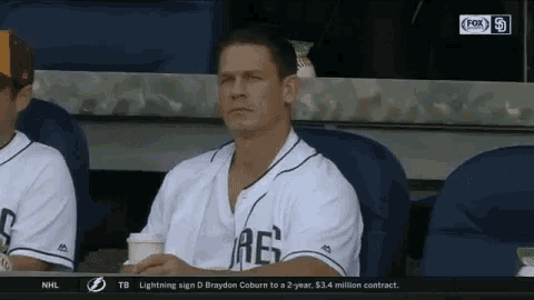 a man in a baseball uniform is sitting in the dugout with a cup of coffee