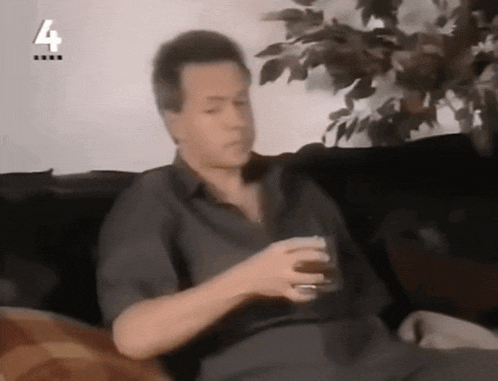 a man sitting on a couch holding a glass with the number 4 on the bottom