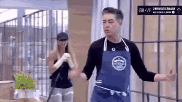 a man in a blue apron is standing in front of a woman in a black shirt .