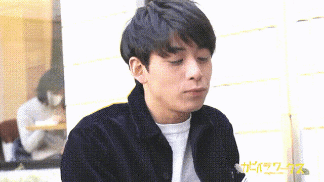 a man in a black jacket and white shirt is eating something with chinese writing on the bottom