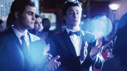 two men in tuxedos are clapping in a dark room