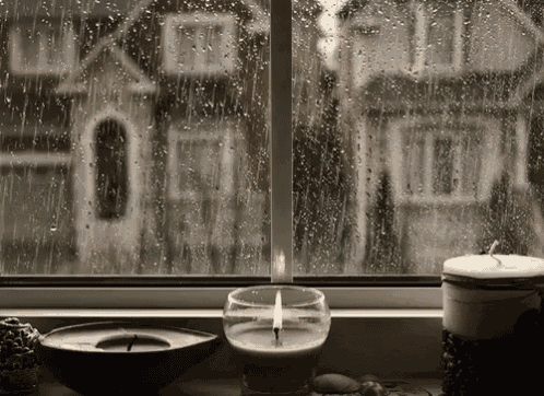 a candle is lit in front of a window with rain drops on the glass