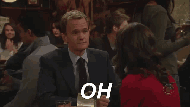 a man in a suit and tie is sitting at a table with a woman and says oh