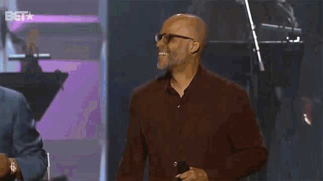 a man wearing glasses stands in front of a microphone with the bet logo in the background