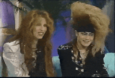 a man and a woman with long hair are sitting next to each other on a couch and smiling .