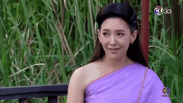 a woman in a purple saree is sitting on a bench in a field .