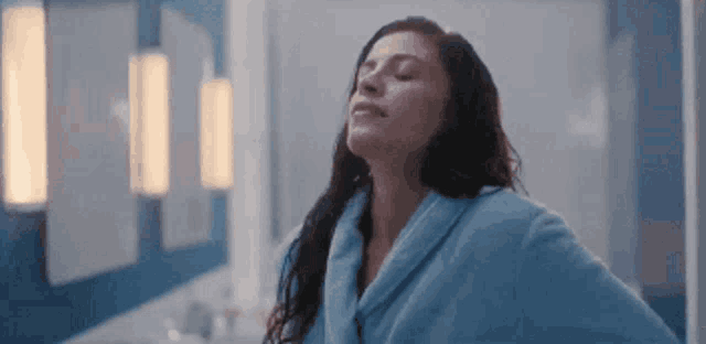 a woman in a bathrobe is standing in front of a mirror in a bathroom .
