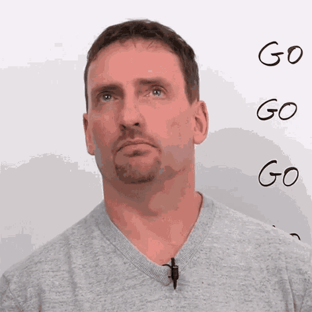 a man in a grey shirt stands in front of a white board with the words go written on it
